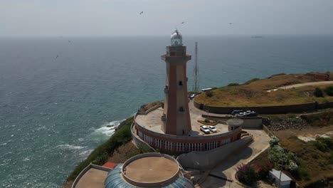 drones en órbita desde la distancia revelando toda la estructura de una marca de tierra, faro de punta ballena y sus cimientos, área de estacionamiento con coches, también otros edificios, porlamar, isla margarita, venezuela