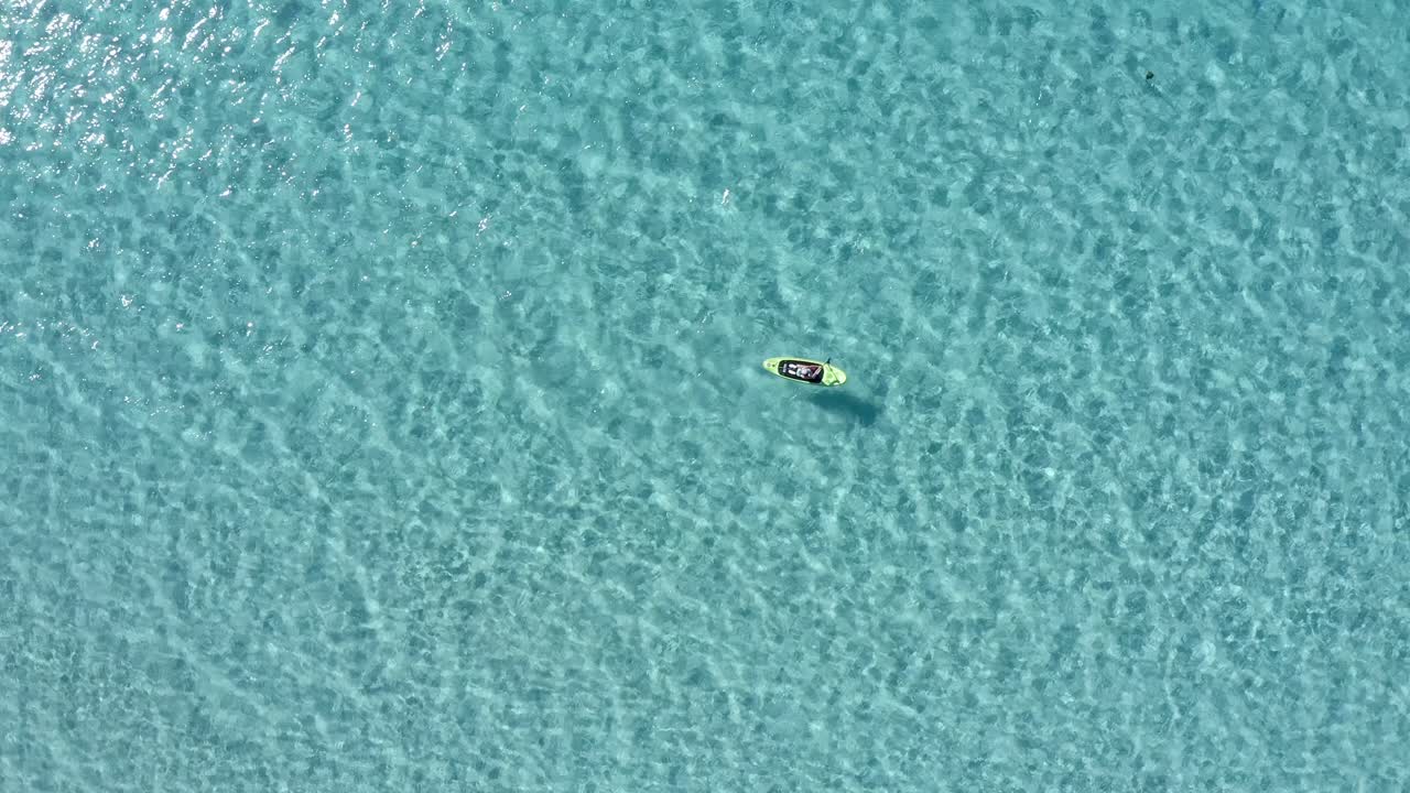 Mid day summer sun reveals a paddle boarder gliding through the calm waters in Spain