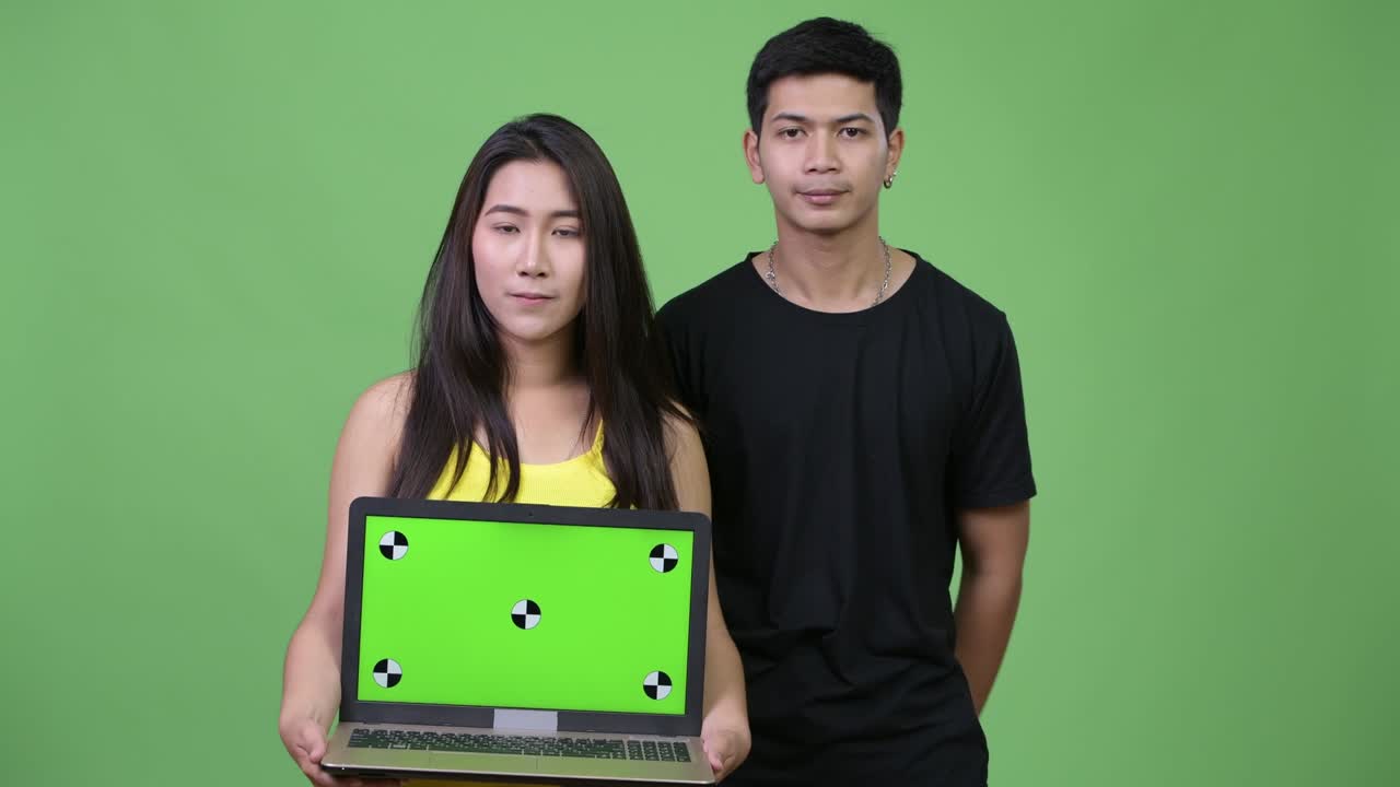 Young Asian couple showing laptop and giving thumbs up