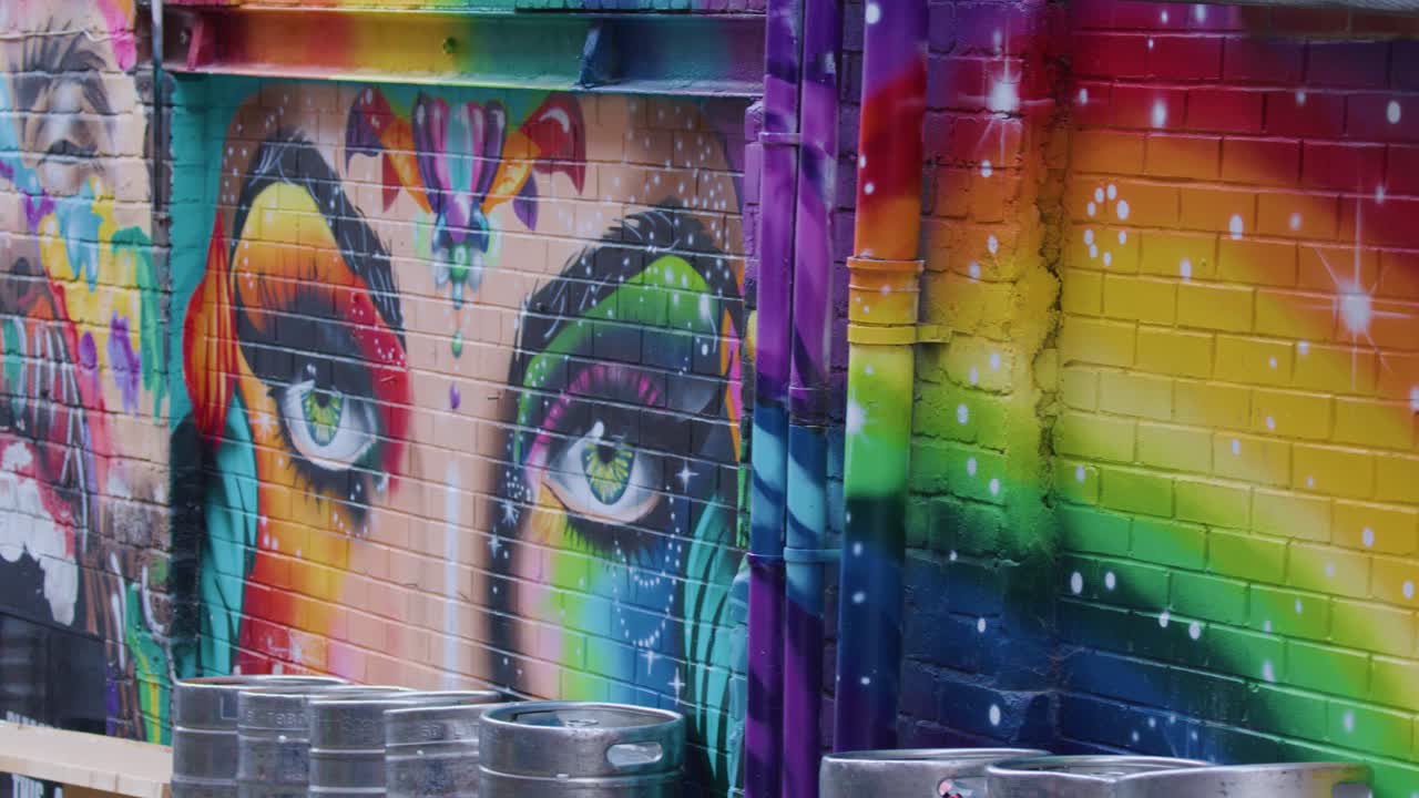 Colorful rainbow mural with expressive eyes, panned by camera in urban Leeds alleyway daylight