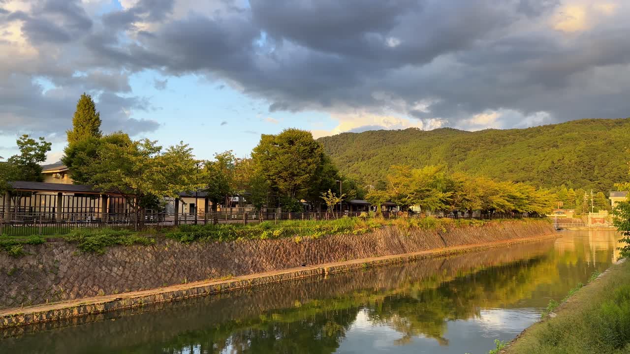 Peaceful Kyoto canal with mountains, trees, reflecting water at sunset