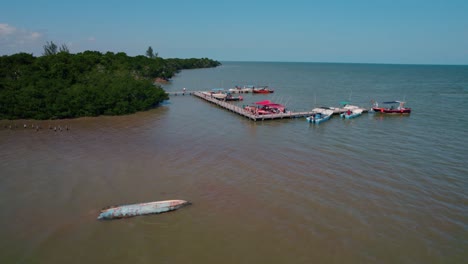 boat dock in lagoon on island holbox in mexico, tourists on wooden dock, parked boats, aerial flyover