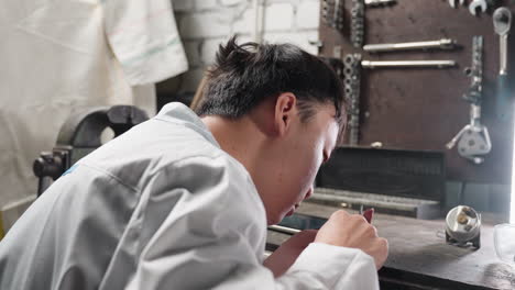 young lab technician works with veiner caliper, adjusting and tapping on tablet in front of a bright light, surrounded by mechanical tools