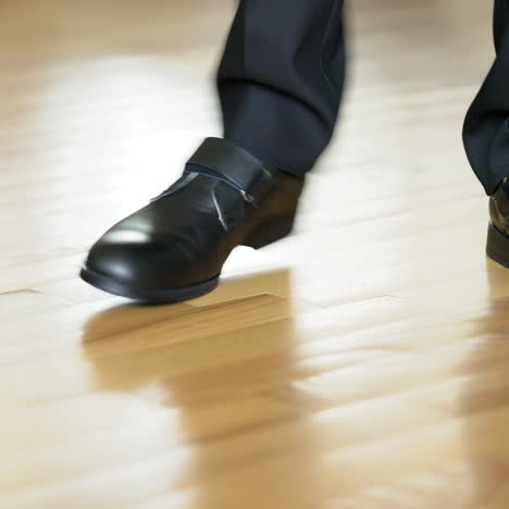 legs of a man in black shoes dancing elements of dubstep on the brown floor background. view shot looking straight at the shoes and legs in black trousers.