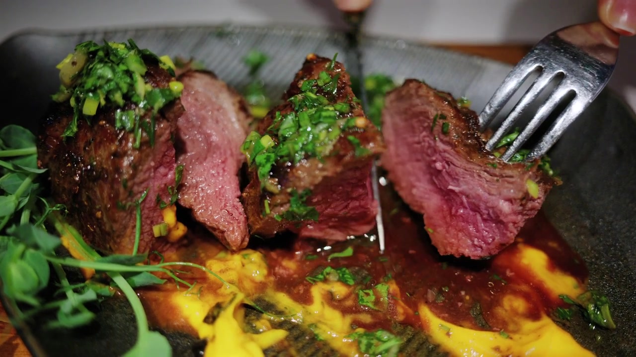Primo piano di una bistecca alla griglia che viene affettata con un coltello e una forchetta in un ristorante.