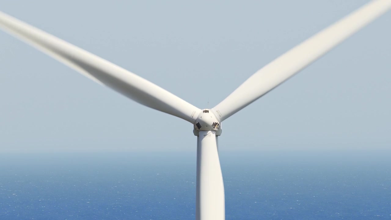 Close-up view of a large wind turbine with its blades spinning against a clear blue sky background, generating clean and renewable electricity from wind power in an offshore wind farm
