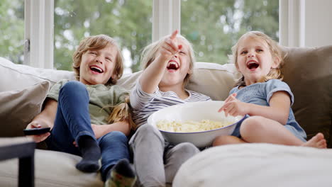 Tres-Niños-Sentados-En-El-Sofá-De-Casa-Riendo-Y-Viendo-Televisión-Con-Palomitas-De-Maíz