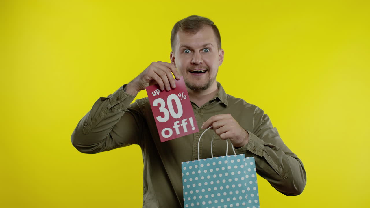 hombre feliz mostrando hasta un 30 por ciento de descuento inscripción de la bolsa de compras, sonriendo, regocijándose descuentos