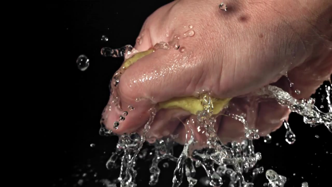 Primer plano de una mano exprimiendo una esponja amarilla mojada con salpicaduras de agua en cámara lenta