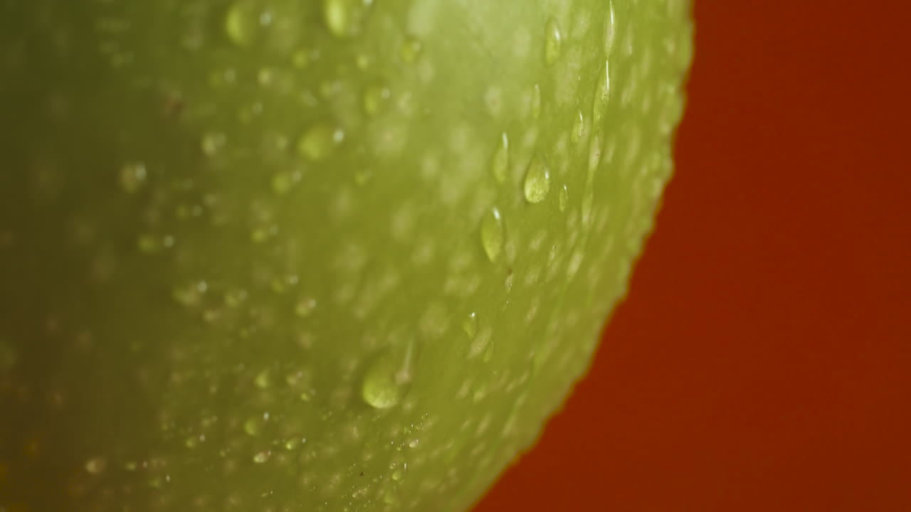 primer plano de una manzana verde con gotas de agua sobre fondo rojo.