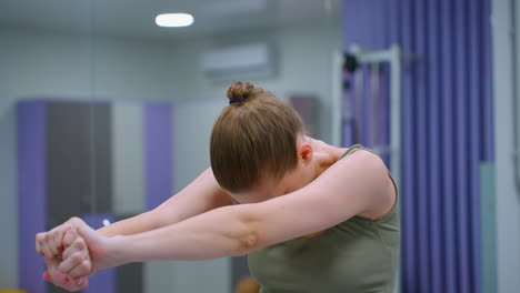 mujer realizando ejercicio de flexibilidad de la columna vertebral en el gimnasio, estirando los brazos hacia adelante, un gran espejo refleja la decoración interior, creando profundidad y simetría, la rutina de fitness se centra en la mejora de la postura
