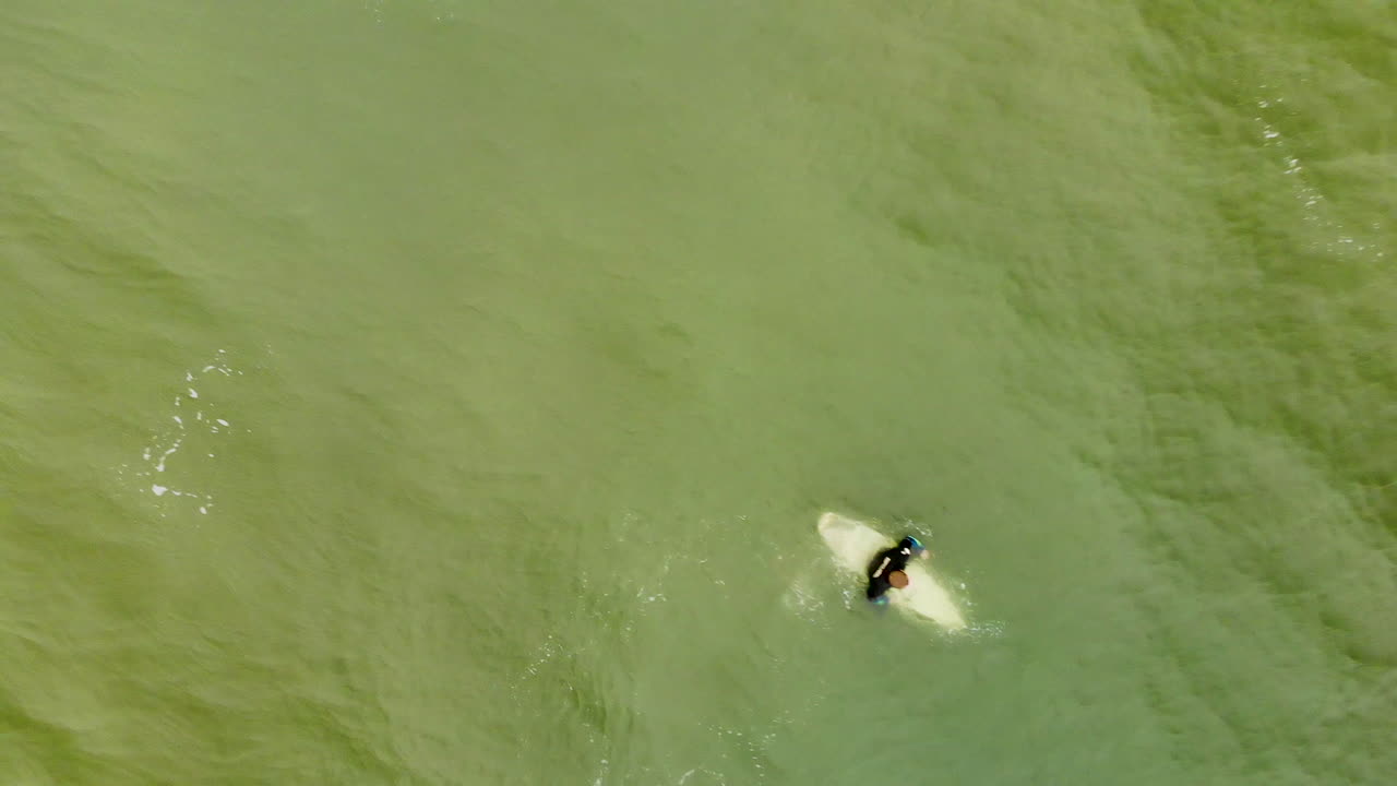 toma aérea de un surfista remando en el océano a través de las olas