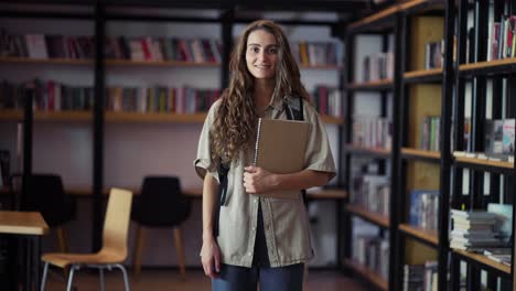 Retrato-De-Una-Mujer-Joven-Y-Bonita-Sonriendo-Feliz-Mirando-La-Cámara-En-El-Fondo-De-La-Estantería-De-La-Biblioteca