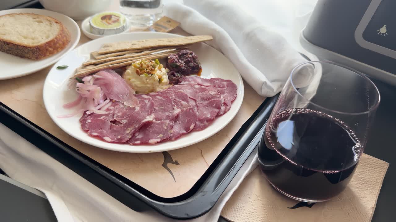 Close-up of premium airplane charcuterie plate with crackers and red wine in soft daylight