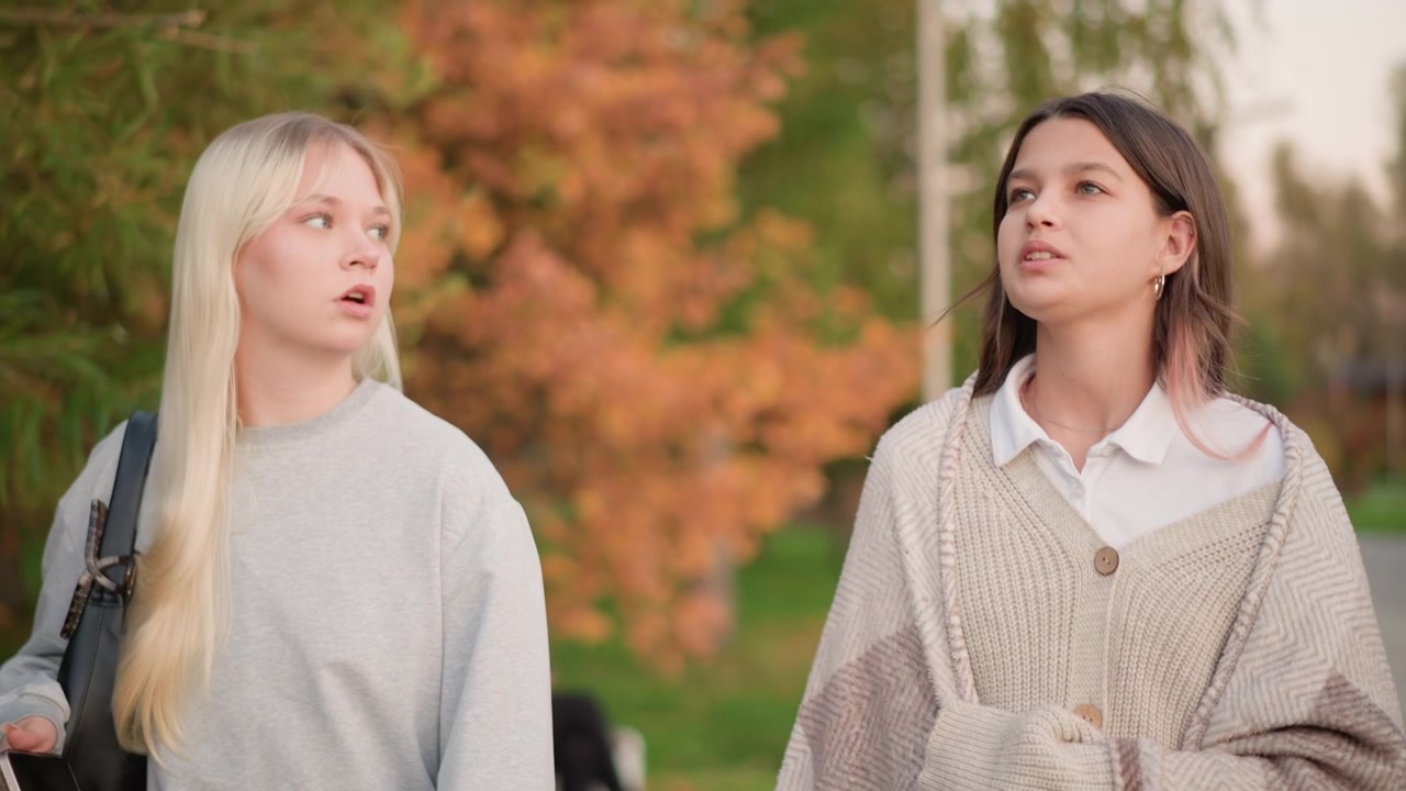 Due giovani donne che camminano e parlano in un parco autunnale.