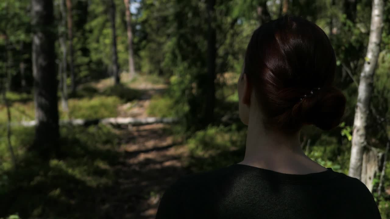 Woman with red hair walking nature forest path peacefully in summer, back rear view