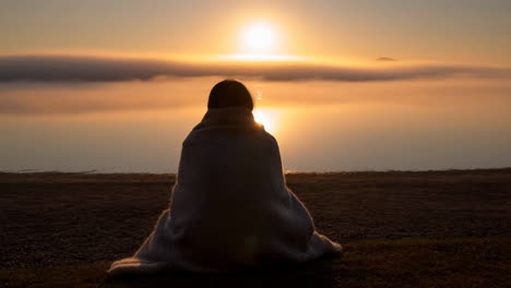 person wrapped in a blanket watching the sunrise over the sea