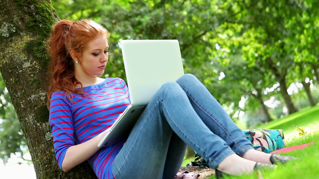 Student sitting against a tree using her laptop