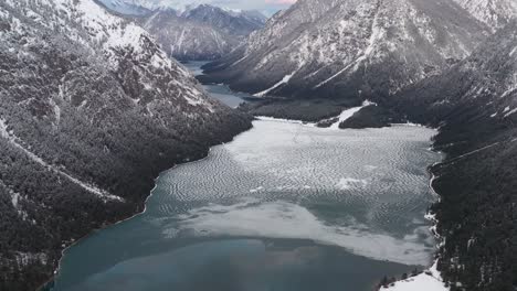 aerial view of partially frozen lake in between snow frosted mountain ranges