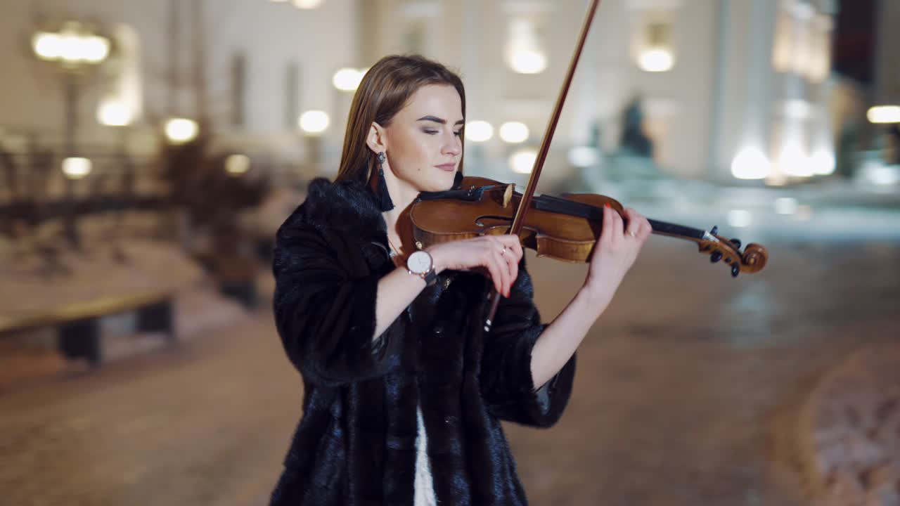 Street artist violinist girl. Young elegant woman violinist playing violin on the street at night