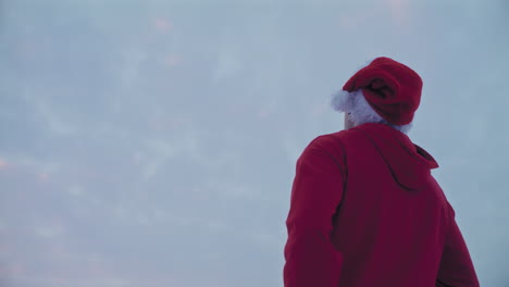 hombre pensativo con chaqueta roja con capucha y sombrero de papá noel mirando al cielo durante la navidad