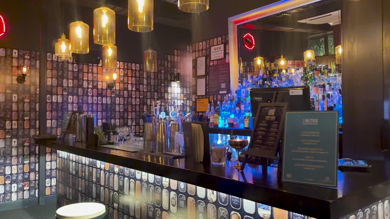 Contemporary bar counter with pendant lighting, neon sign, and colorful bottles in moody evening ambiance