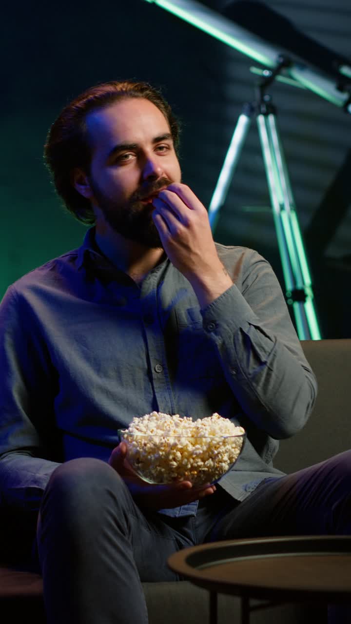 Vertical video Man turning on TV using remote control, eating popcorn