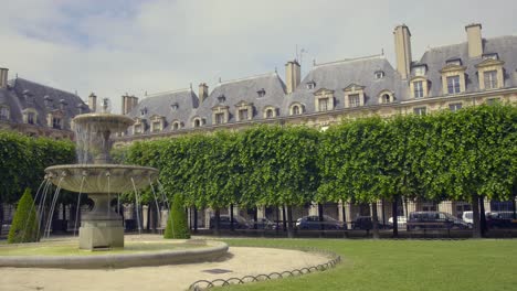 one of the fountains at square louis xiii in place des voges, paris, france with houses in background