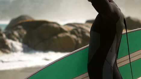 man in wet suit holding surfboard