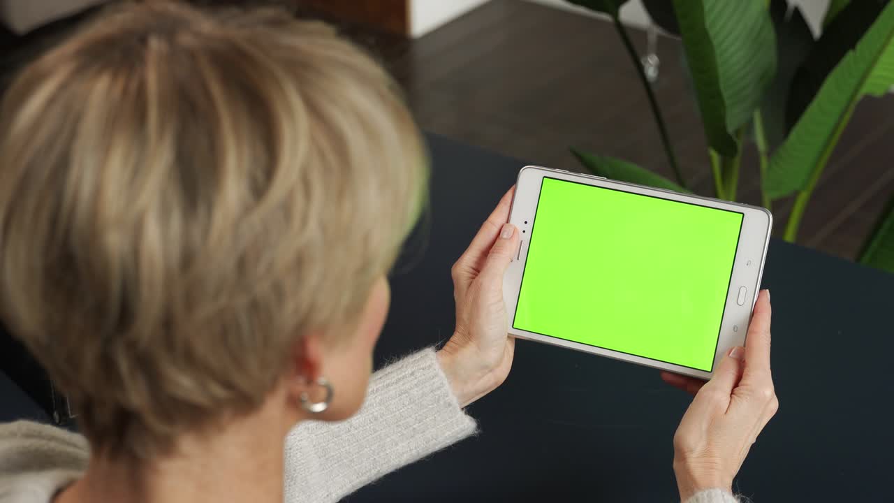 una mujer de mediana edad está viendo contenido usando una tableta en una pantalla verde
