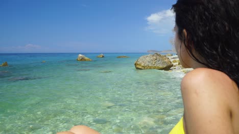 orilla del mar con agua esmeralda cristalina que lava los acantilados y una chica viendo el paisaje marino del paraíso de vacaciones