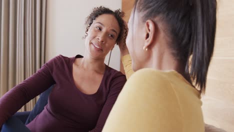 Happy-biracial-lesbian-couple-relaxing-on-couch-together,-smiling-and-talking,-in-slow-motion