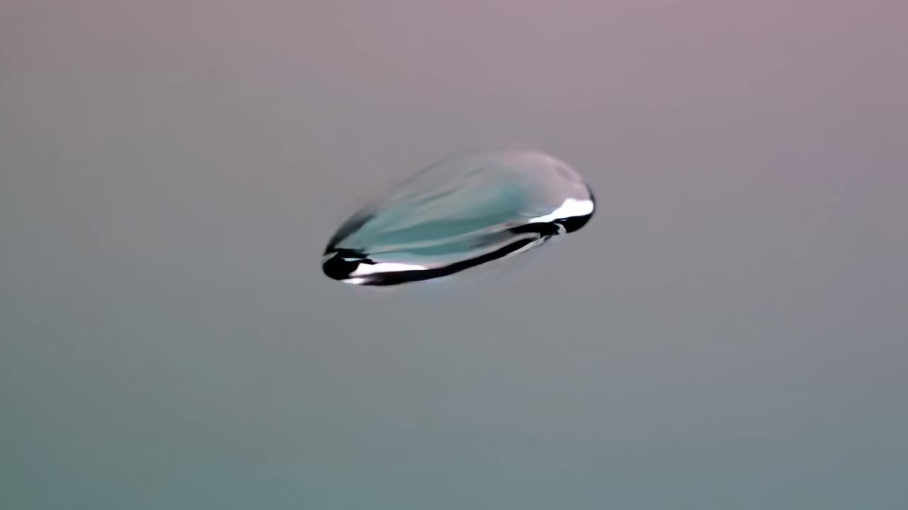 Close-up video of a single water droplet suspended mid-air against a soft gradient background