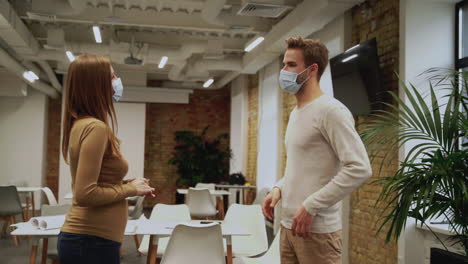 young woman and man wear face masks, practice social distancing and talk about work with in the office