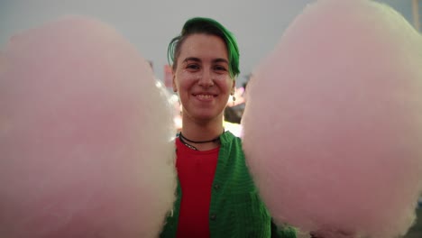 Retrato-De-Una-Chica-Lesbiana-Con-Un-Corte-De-Pelo-Corto-De-Color-Verde-Y-Brillos-En-La-Cara-Que-Sostiene-Dos-Enormes-Algodones-De-Azúcar-En-Un-Parque-De-Atracciones.