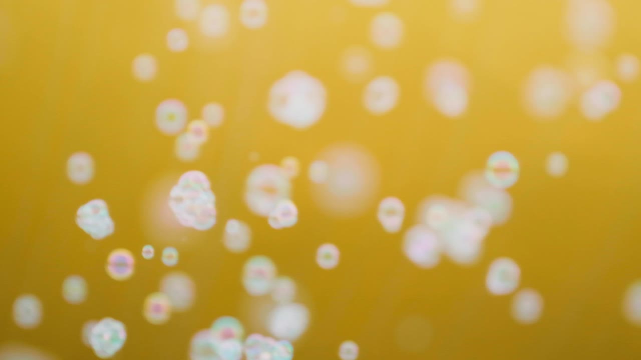 색 비누 거품이 노란색 배경에서 느린 동작으로 날아다닙니다.