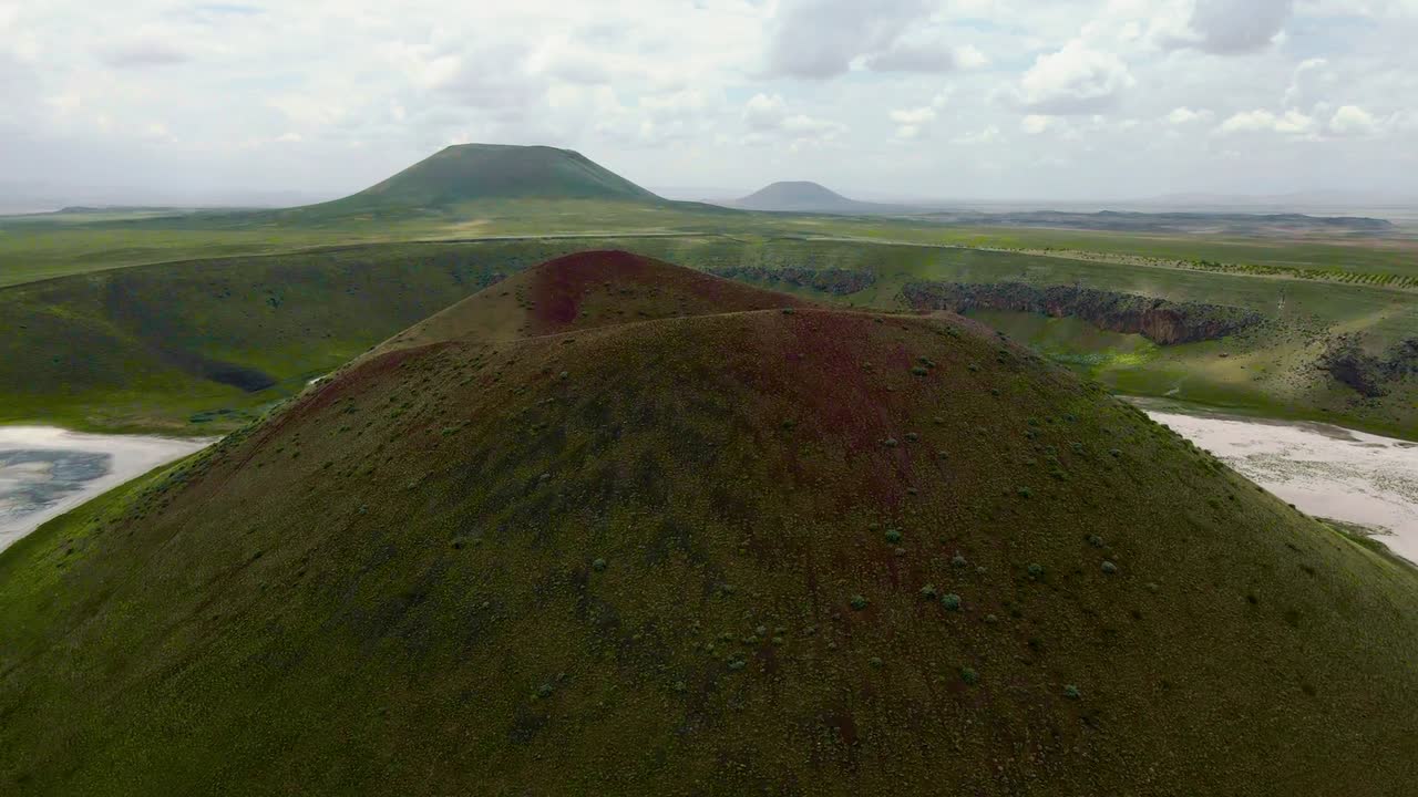 Drone view of mossy volcanic craters and wide green plains in Iceland showing layered landscape, distant peaks, old lava formations, and sky filled with clouds on a bright summer day