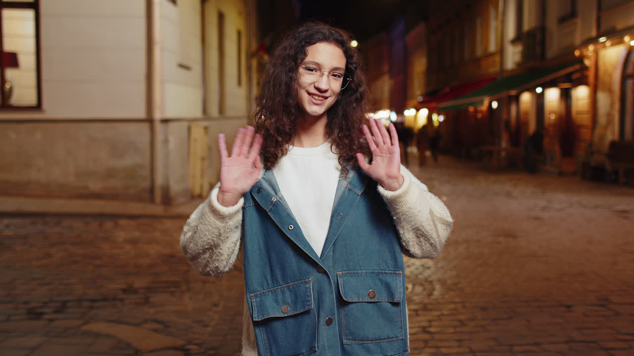 adolescente agitando las manos gestando hola saludos o adiós en la calle de la ciudad urbana por la noche