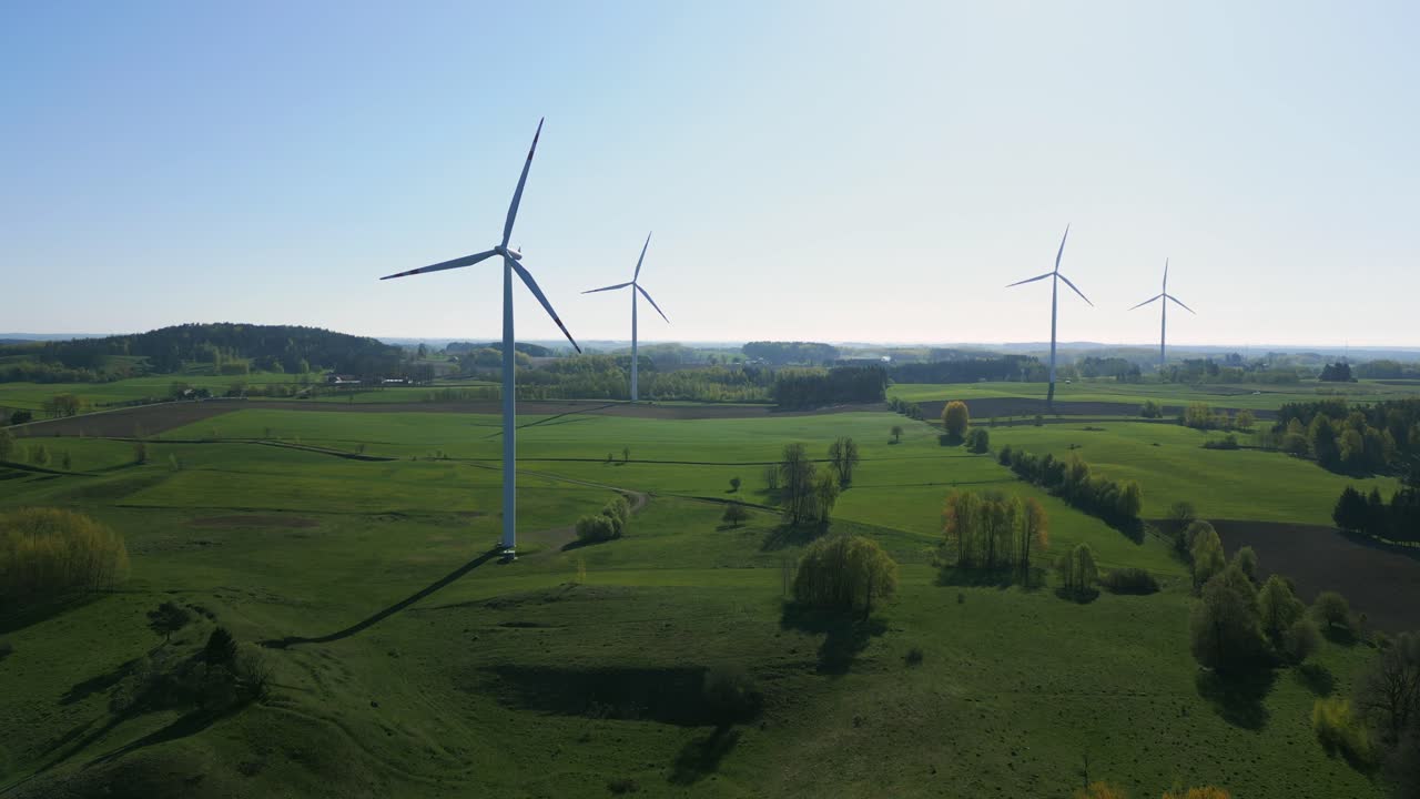 Aerial view of a wind turbine farm in a green landscape. The camera is slowly moving away