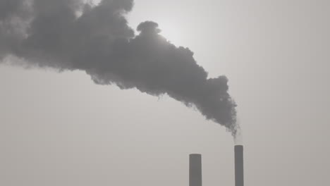 slowmotion shot of industrial smoke from a chimney going up in the air with the sun shining through in the background log