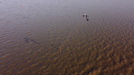 aerial tracking shot of kitesurfer kite-boarding with speed over dirty river at sunset time