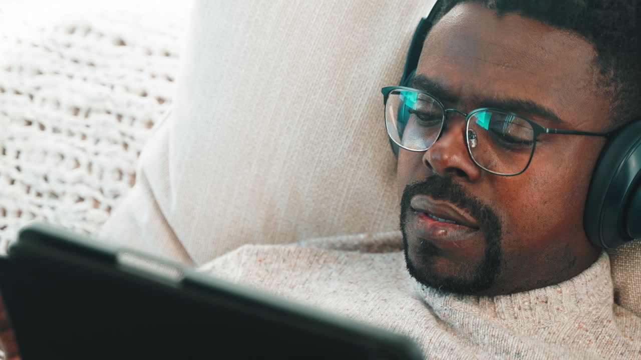 Man relaxing on a couch, listening to music and watching videos on a tablet