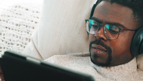 man relaxing on a couch, listening to music and watching videos on a tablet