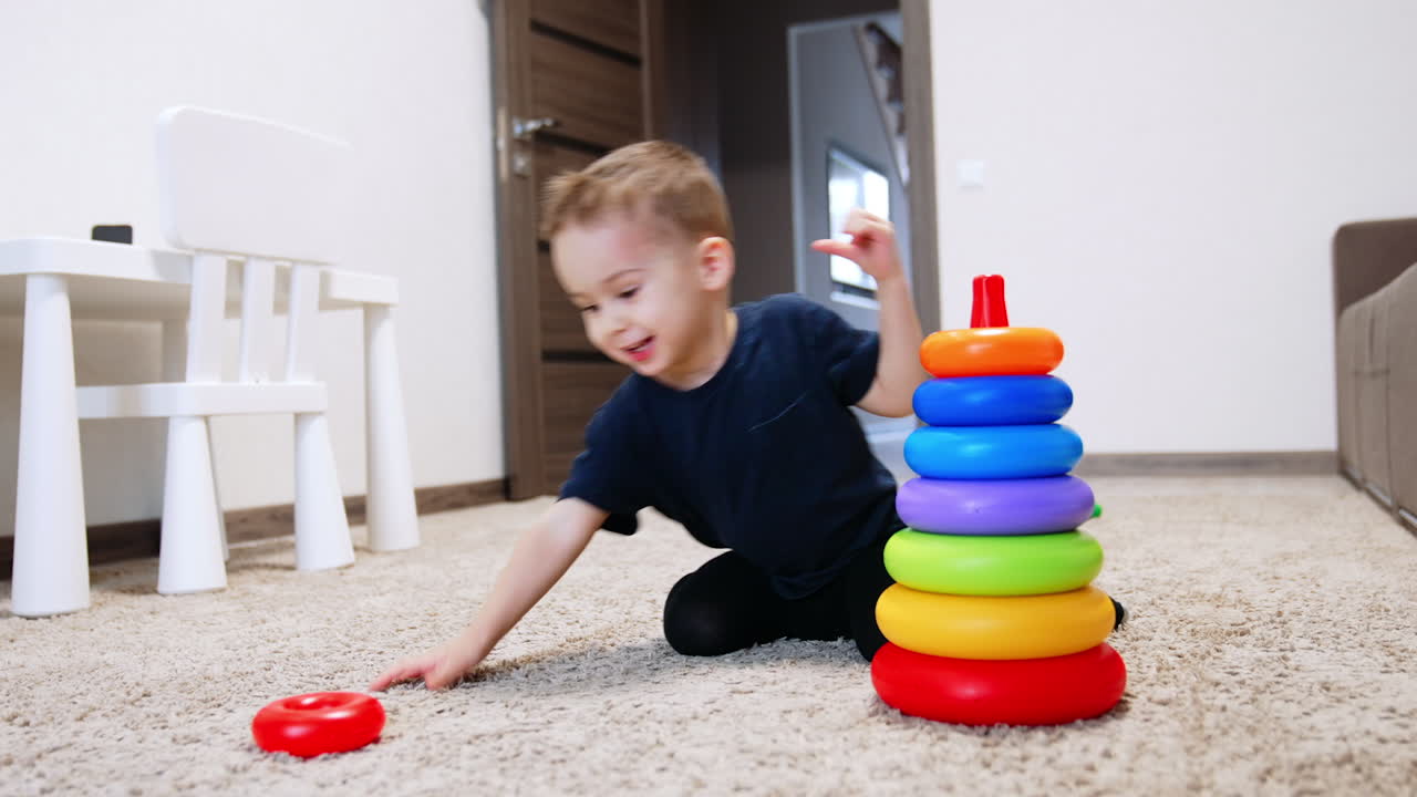 Happy Caucasian toddler building a toy pyramid cheerfully. Cute smiling baby boy playing at home.