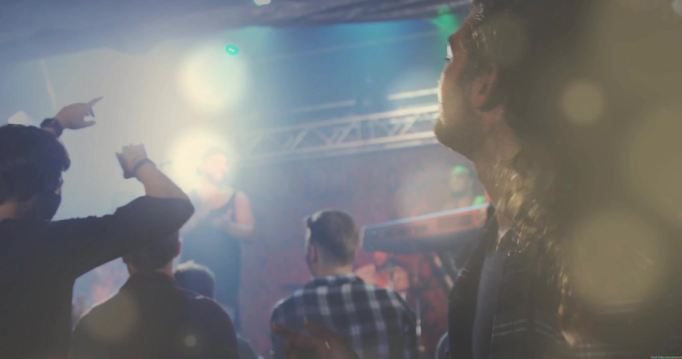 Uomo con capelli lunghi che scuote i capelli sul palco musicale, con bagliori animati dell'obiettivo che pulsano mentre la folla reagisce ai tasti