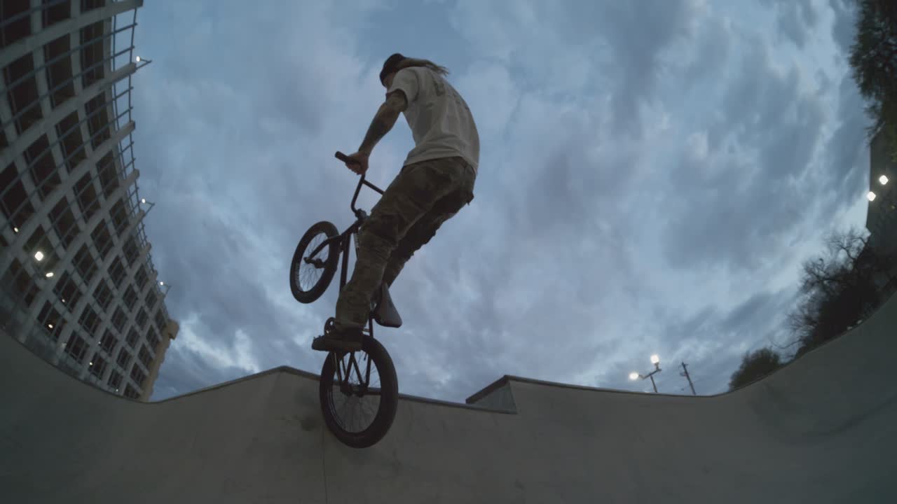 BMX biker tweaking huge air out of skatepark bowl at sunrise, fisheye follow at 800fps extreme slowmo