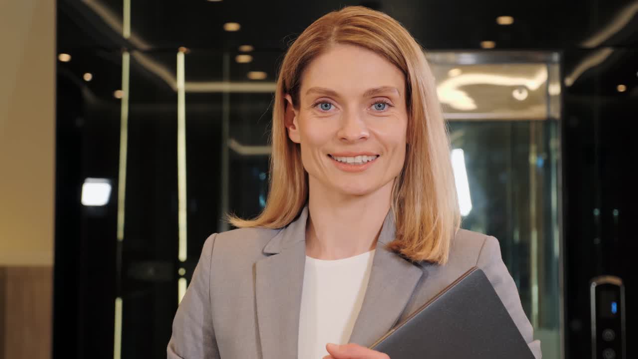 Businesswoman smiling in office hall. Attractive adult business woman model looking at camera, happy beautiful blonde lady professional pretty face dental smile posing stand alone indoors, portrait.