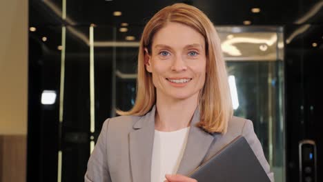 businesswoman smiling in office hall. attractive adult business woman model looking at camera, happy beautiful blonde lady professional pretty face dental smile posing stand alone indoors, portrait.