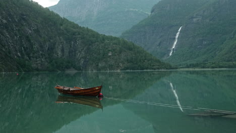 stunning view of a wooden rowing boat attached on a buoy on a beautiful calm lake in a norwegian fjord with intense water reflections, norway, mountains