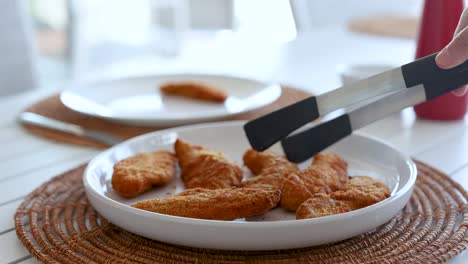 a sequence of serving fried chicken pieces onto a plate using tongs on a set dining table